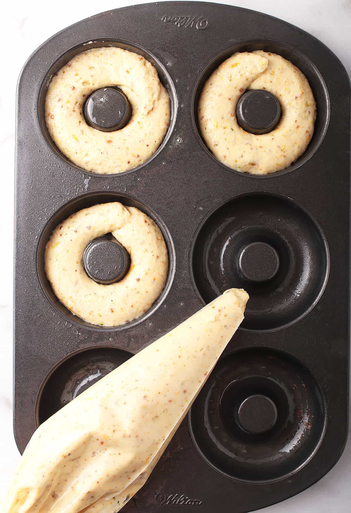 Piped doughnut batter into a doughnut tin