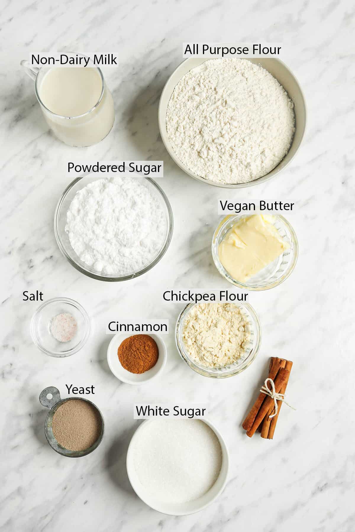 All the ingredients for the cinnamon rolls measured out and placed in small containers on a marble countertop. 