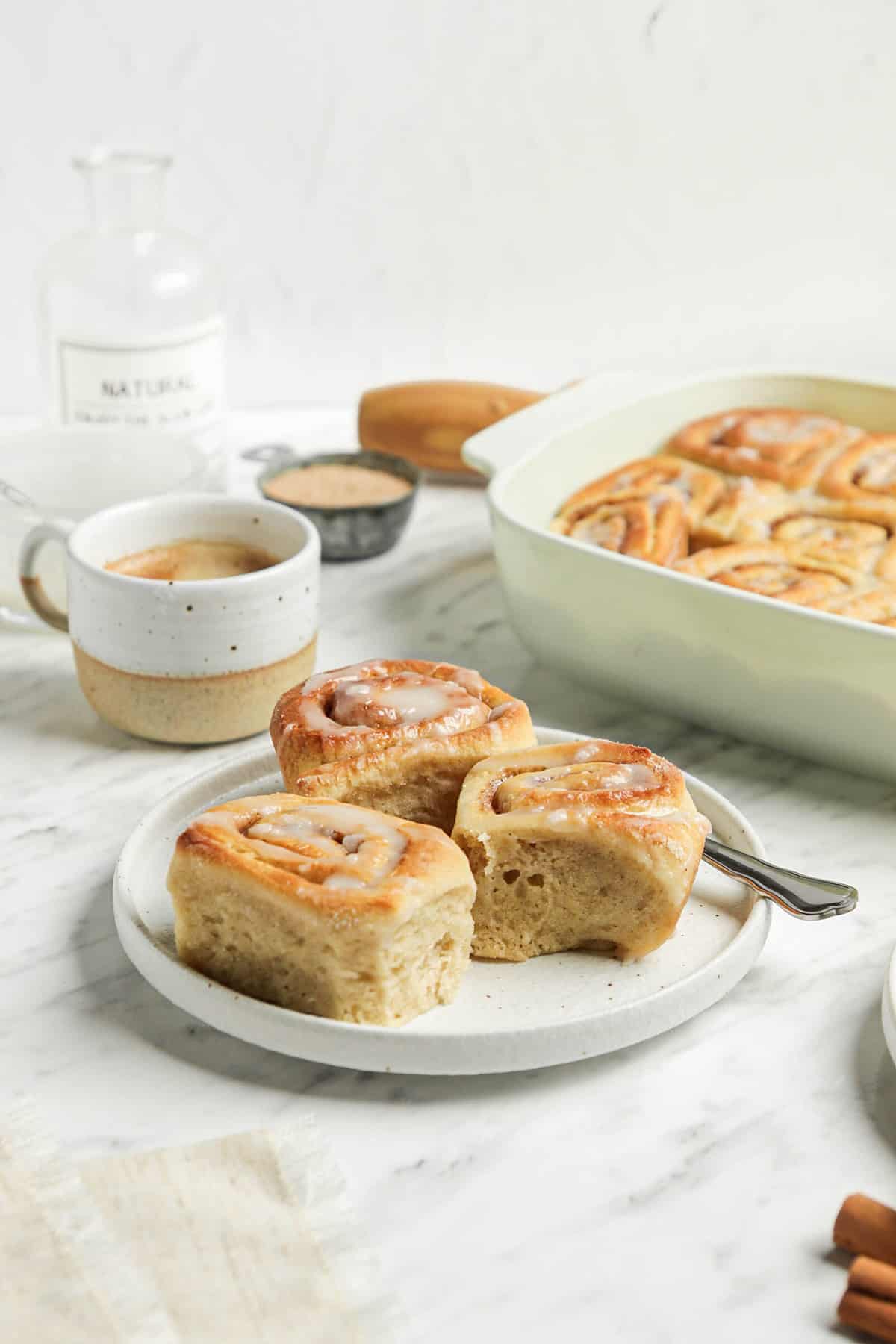 3 finished cinnamon rolls on a white plate with a fork and a cup of coffee. 