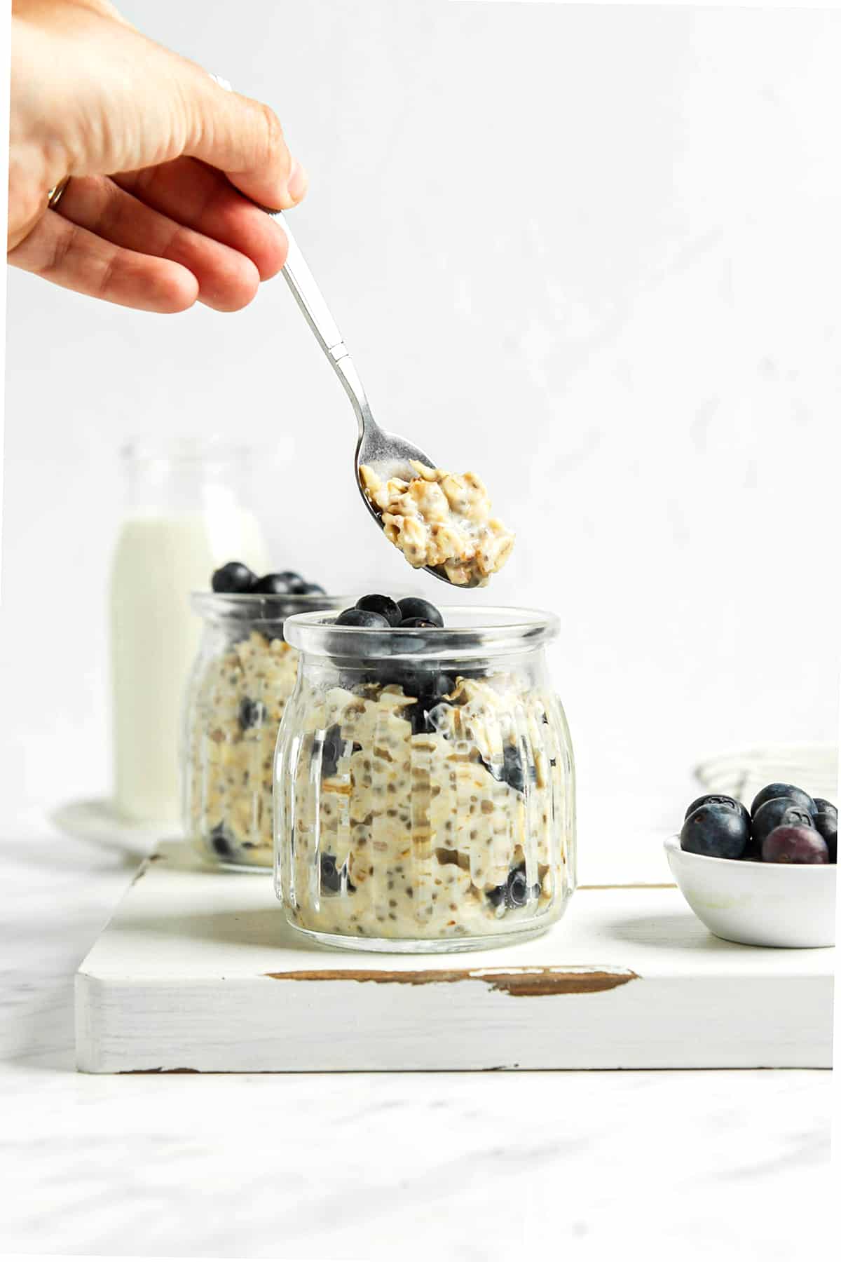 Hand holding a spoonful of overnight oats over finished oats. 