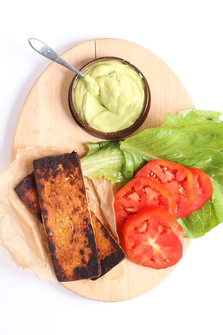 Lettuce, tomato, tofu bacon, and avocado mayo on a oval wooden board