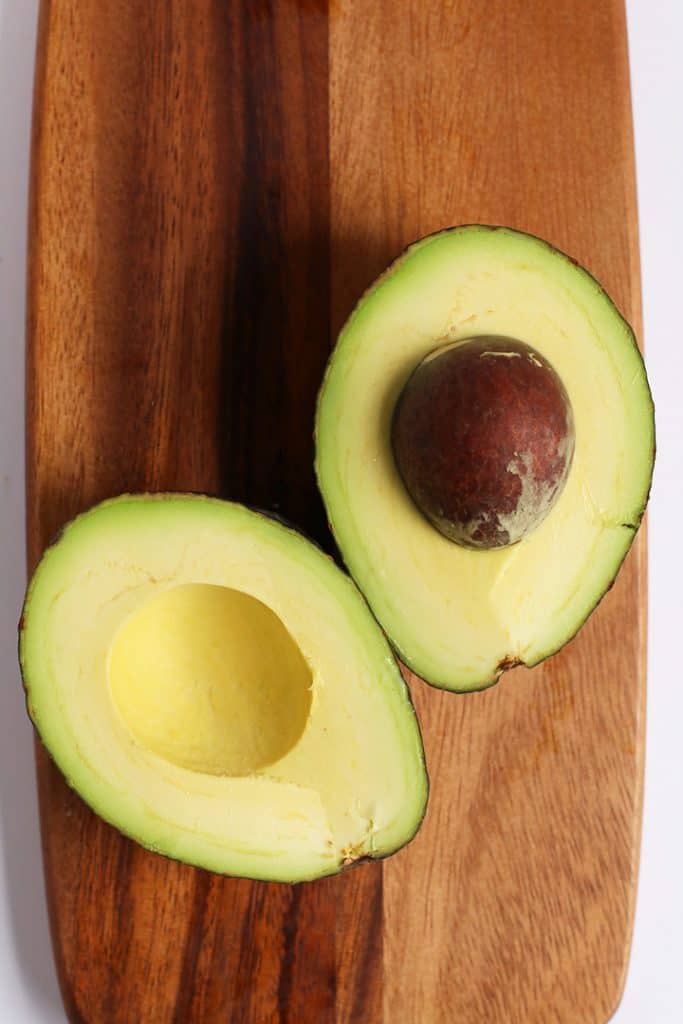 An avocado cut in half on a wooden board