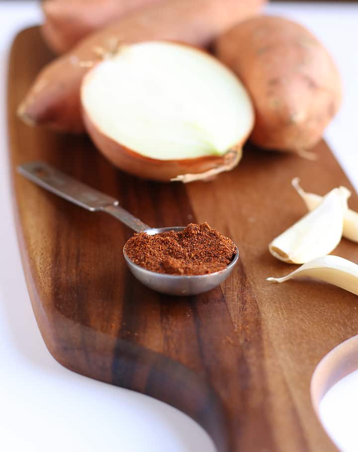 Onion, sweet potatoes, and chili powder on wooden board