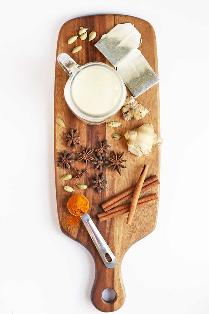 Glass of milk, whole spices, and black tea bags on a wooden board