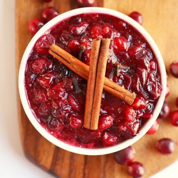 Finished cranberry sauce in a white bowl with two cinnamon sticks