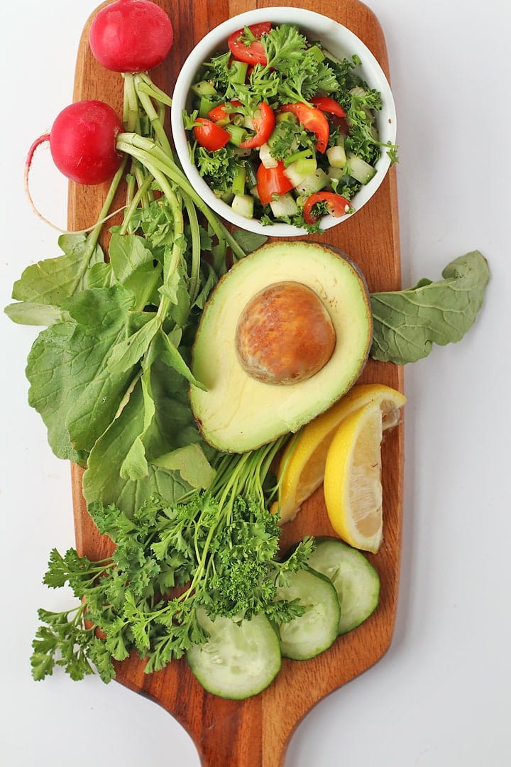 Avocado, parsley, cucumbers, and radishes on a wooden board