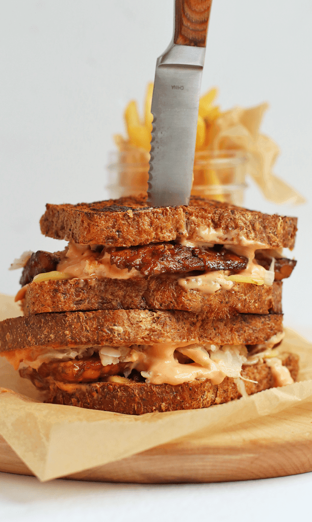 Vegan Rueben Sandwich stacked on top of one another with a fork through the middle. 