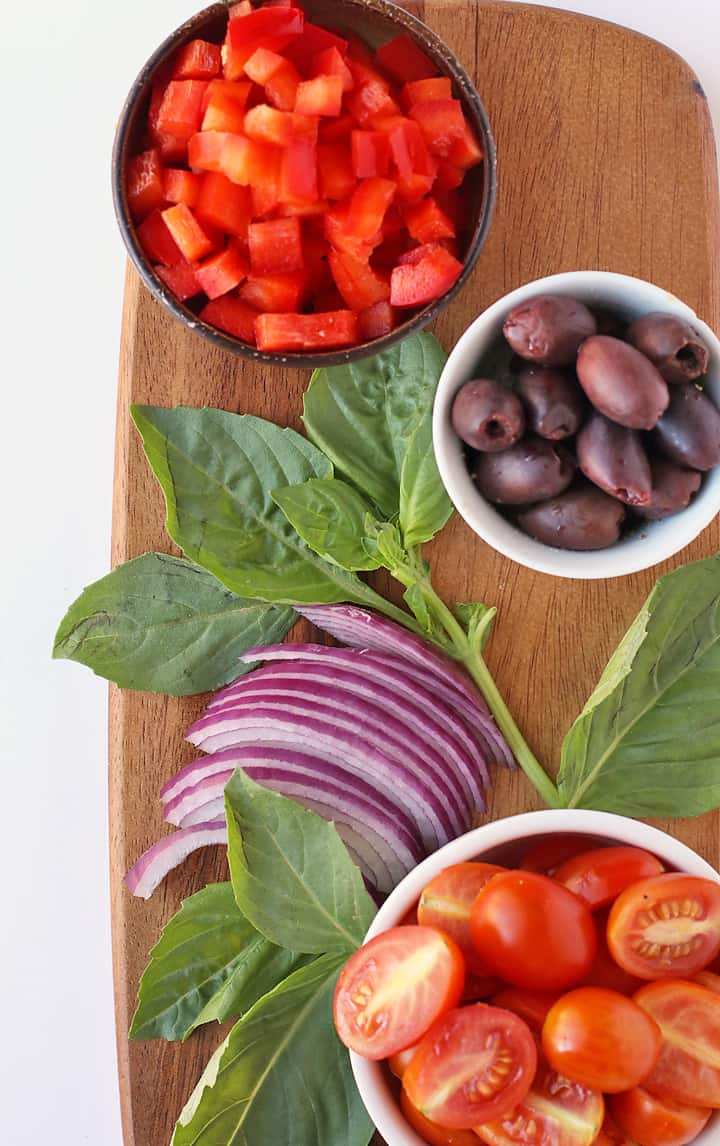 Olives, peppers, onions, and basil on a wooden platter