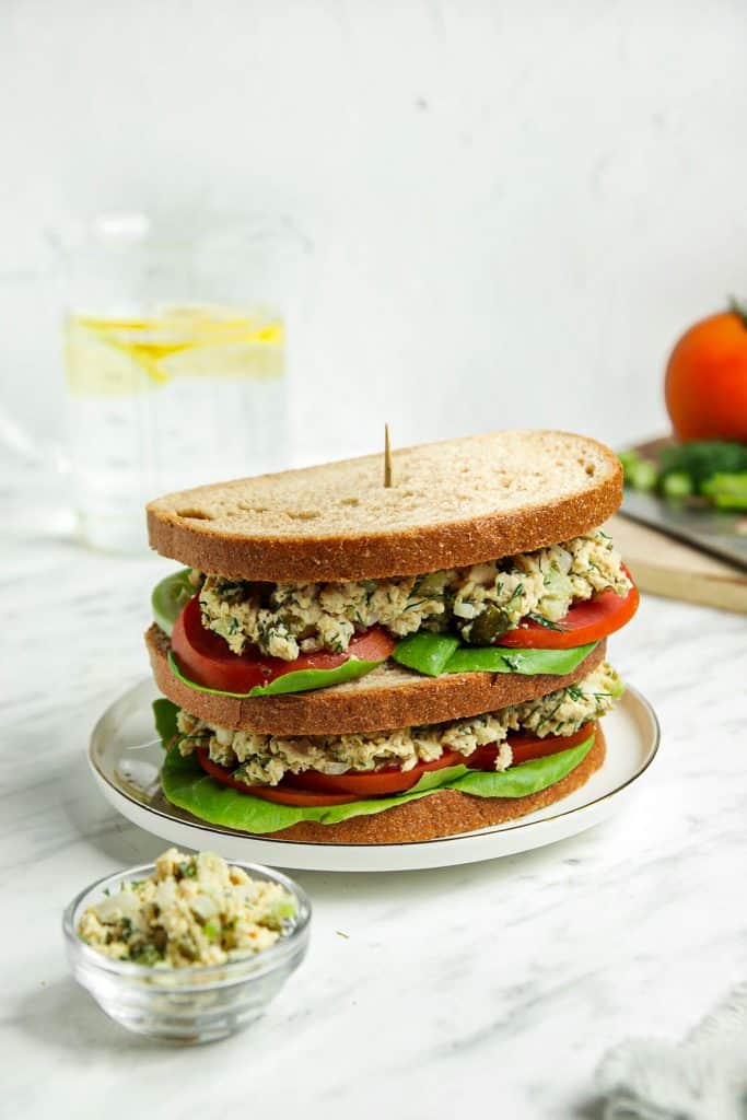 Finished vegan Tuna Salad sandwich with tomatoes and lettuce on a white plate 