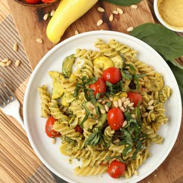 Vegan pesto pasta on a white plate with cherry tomatoes