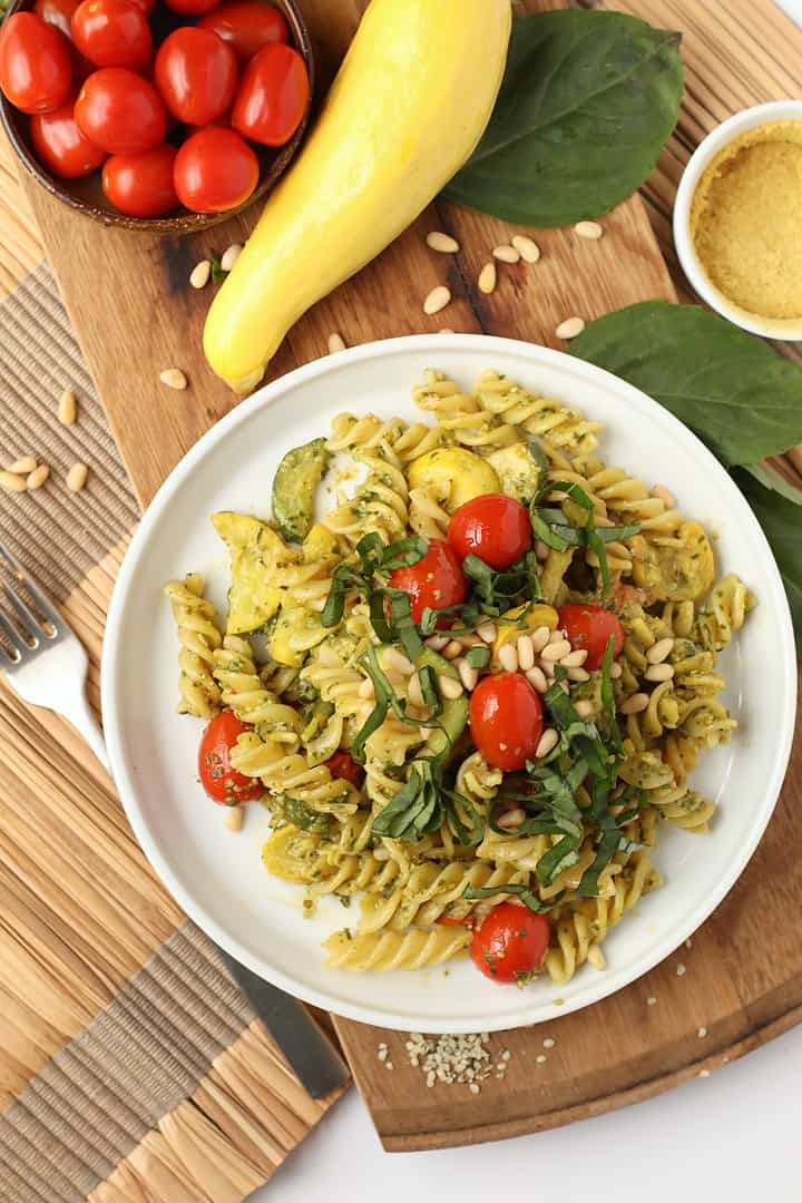 Vegan pesto pasta on a white plate with cherry tomatoes