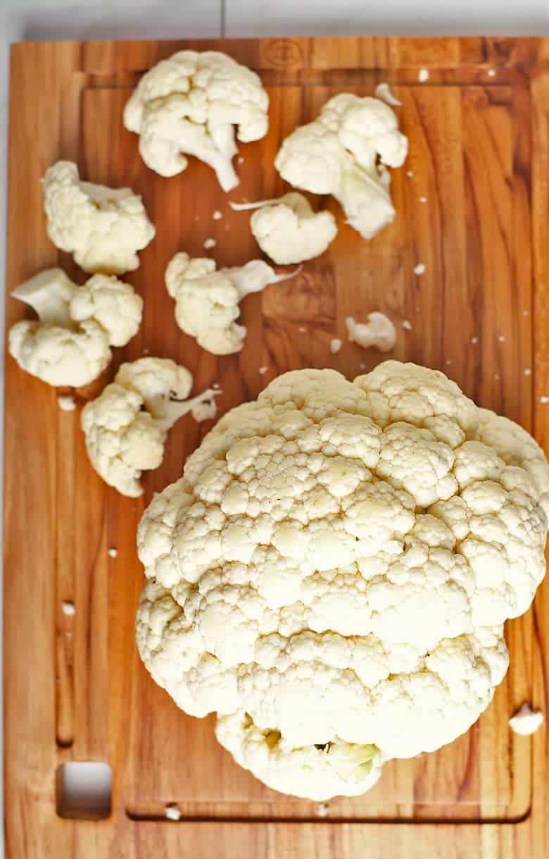 Head of cauliflower with broken florets on a cutting board