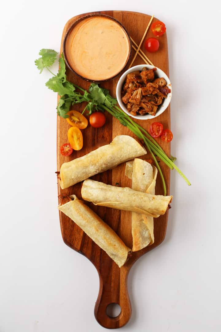 Vegan taquitos on a platter with creamy dipping sauce