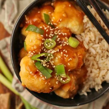 Baked Orange Cauliflower and rice in a black bowl with chopsticks