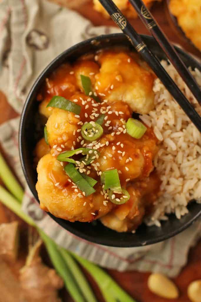 Baked Orange Cauliflower and rice in a black bowl with chopsticks