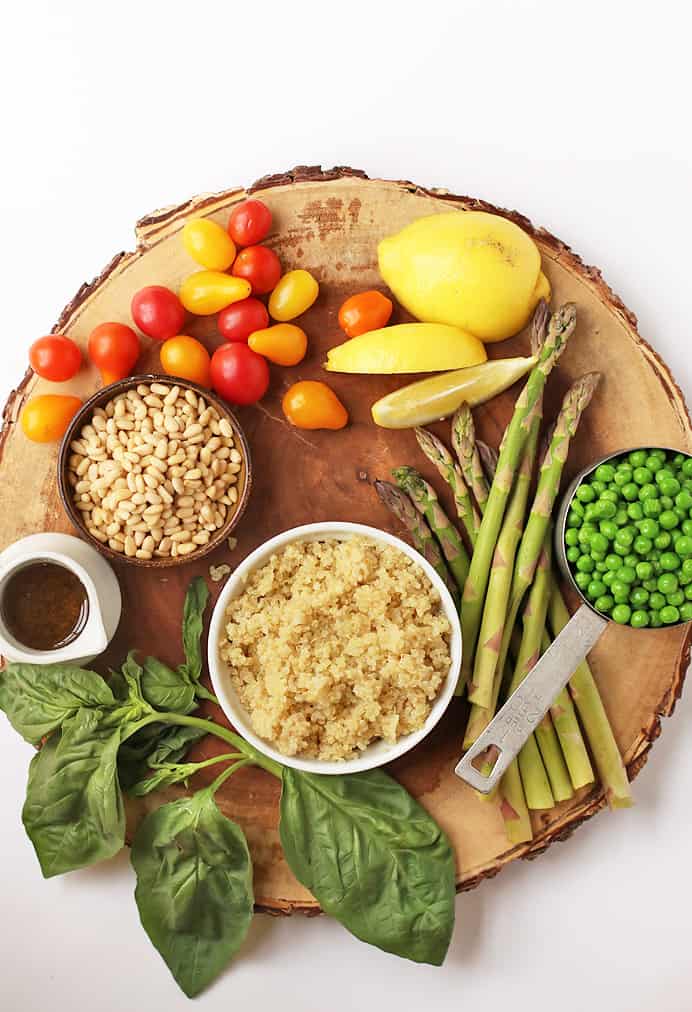 Quinoa, veggies, pine nuts, and fresh basil on a wooden platter