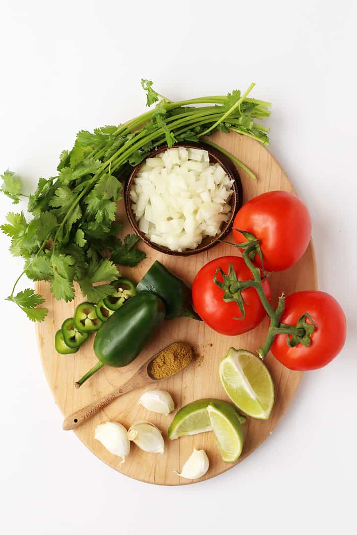 Tomatoes, lime, garlic, jalapeño, and diced onion on a wooden board