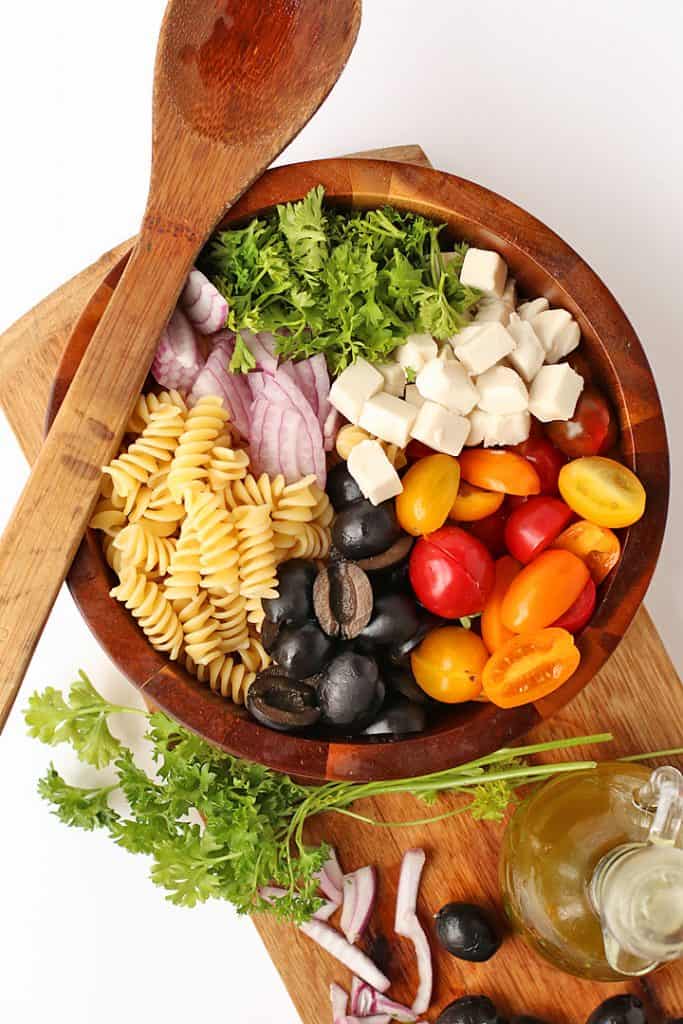 Plant-based pasta salad ingredients in a wood bowl with vegan dressing
