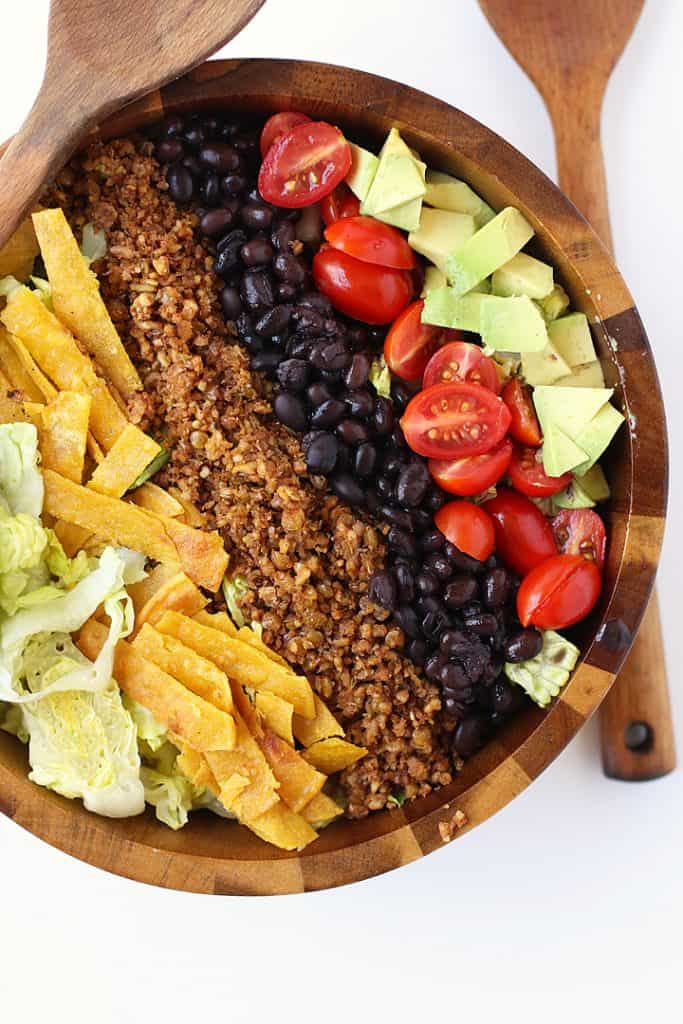 Close-up of vegan taco salad with romaine, beans, and avocado served in a wooden bowl
