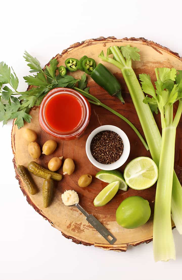 Celery, tomato juice, pickles, and lime on a wooden platter