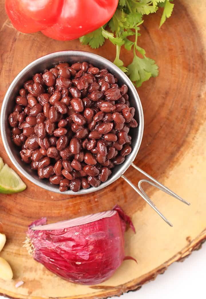 Cooked black beans in a small bowl next to cilantro and onions