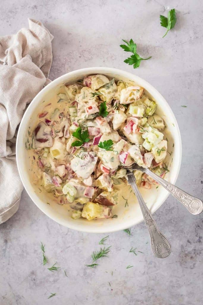 Creamy vegan potato salad in a white bowl with spoons