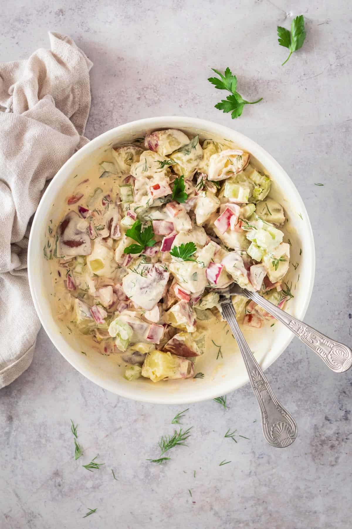 Finished potato salad in a white bowl with two metal spoons