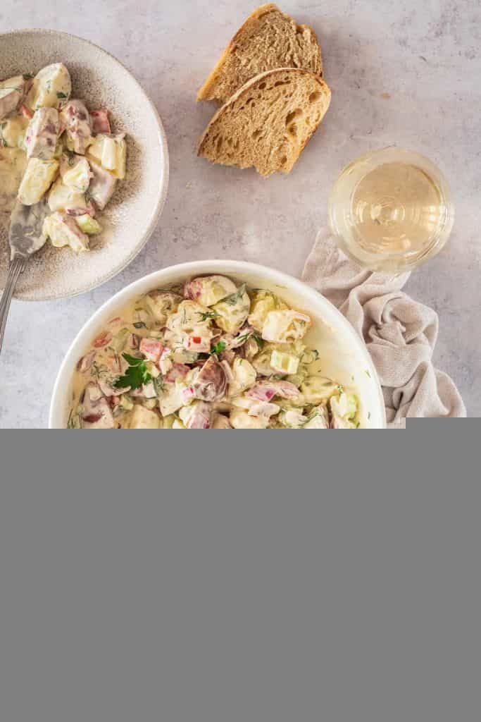 Finished salad in a white bowl with a serving spoon next to a glass of white wine. 