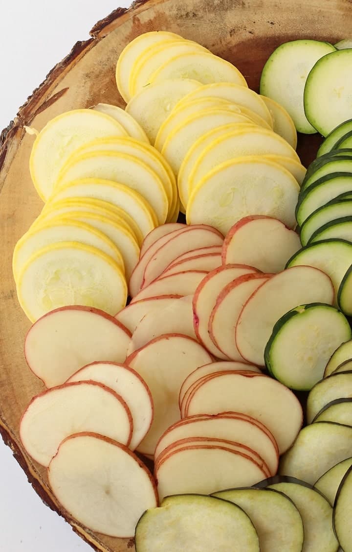 Thinly sliced zucchini, squash, and potatoes on cutting board