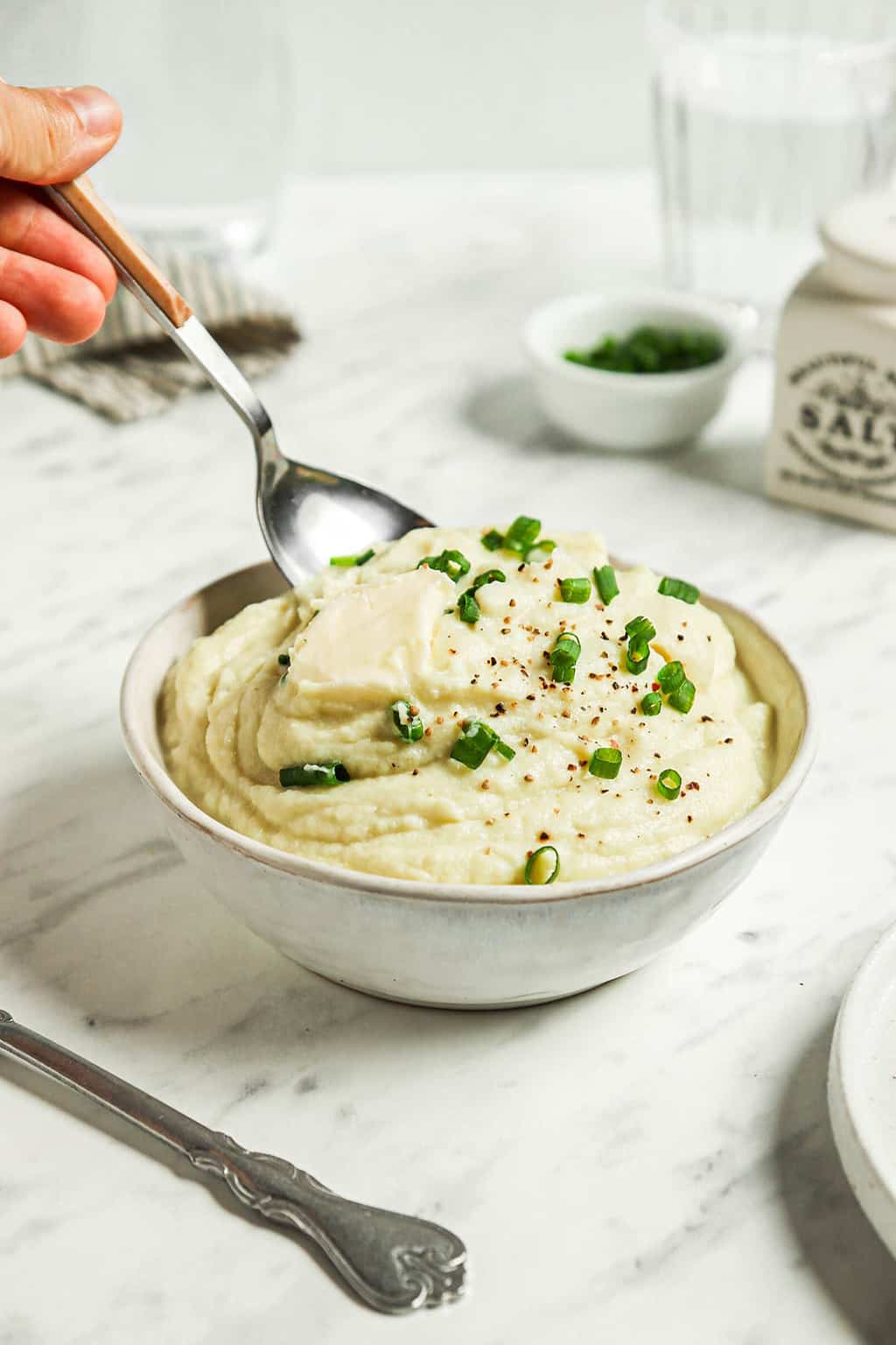 Finished cauliflower mash in a large white bowl with a spoon