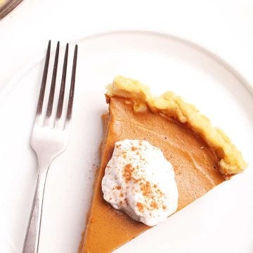 Slice of vegan Pumpkin Pie with coconut whipped cream and cinnamon.