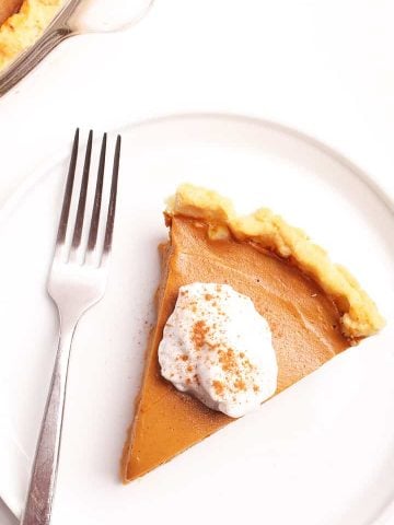 Slice of vegan Pumpkin Pie with coconut whipped cream and cinnamon.