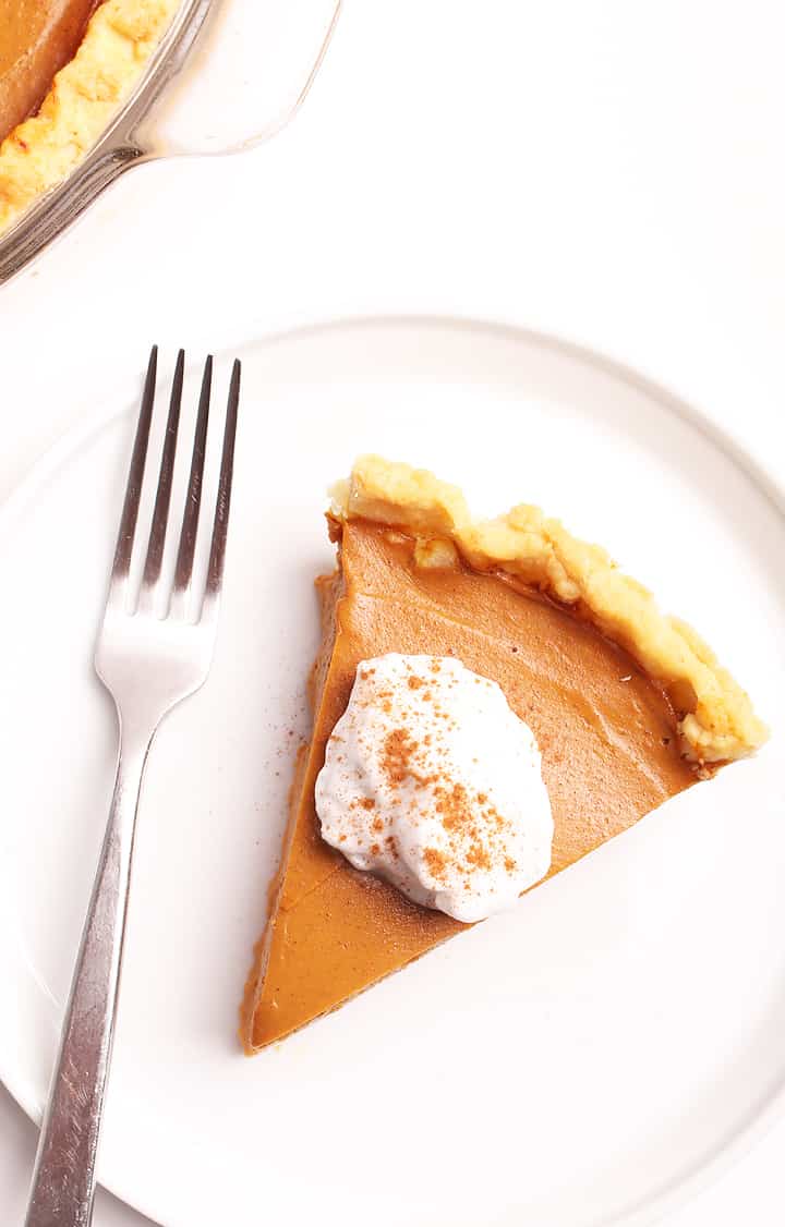 Slice of vegan Pumpkin Pie with coconut whipped cream and cinnamon.