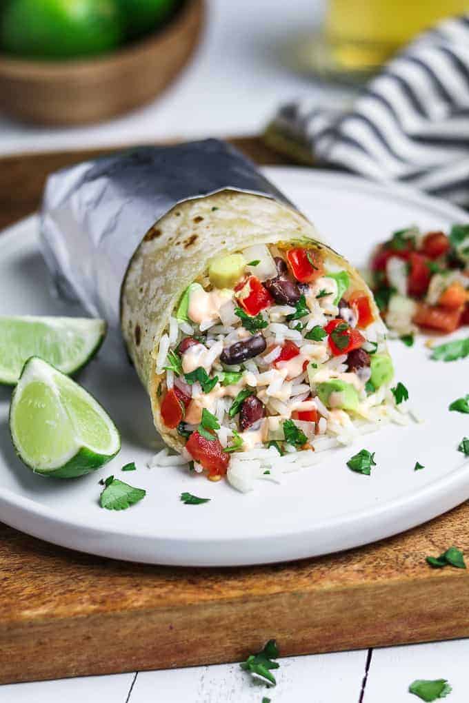 Vegan burrito wrapped in foil and served on a white plate