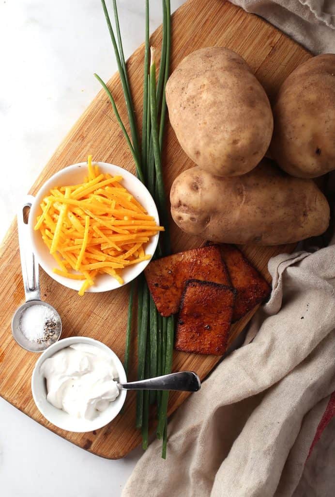 Russet potatoes, cheese, chives, and tofu bacon on a wooden board