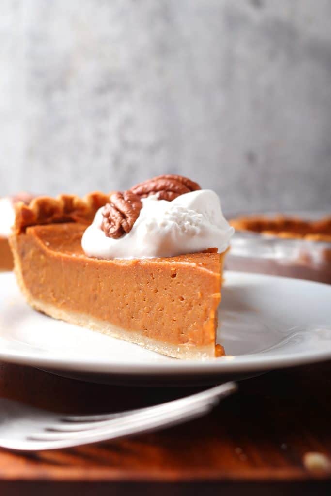 Slice of sweet potato pie with coconut whipped cream on a white plate