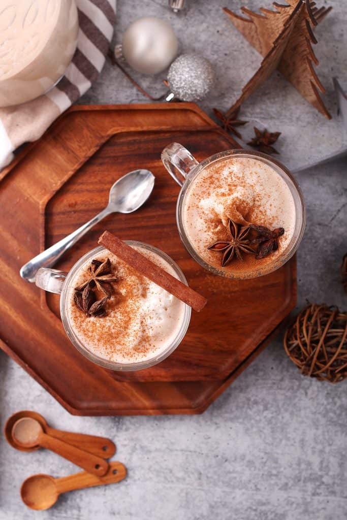 Two glasses of eggnog with whole spices on a wooden platter