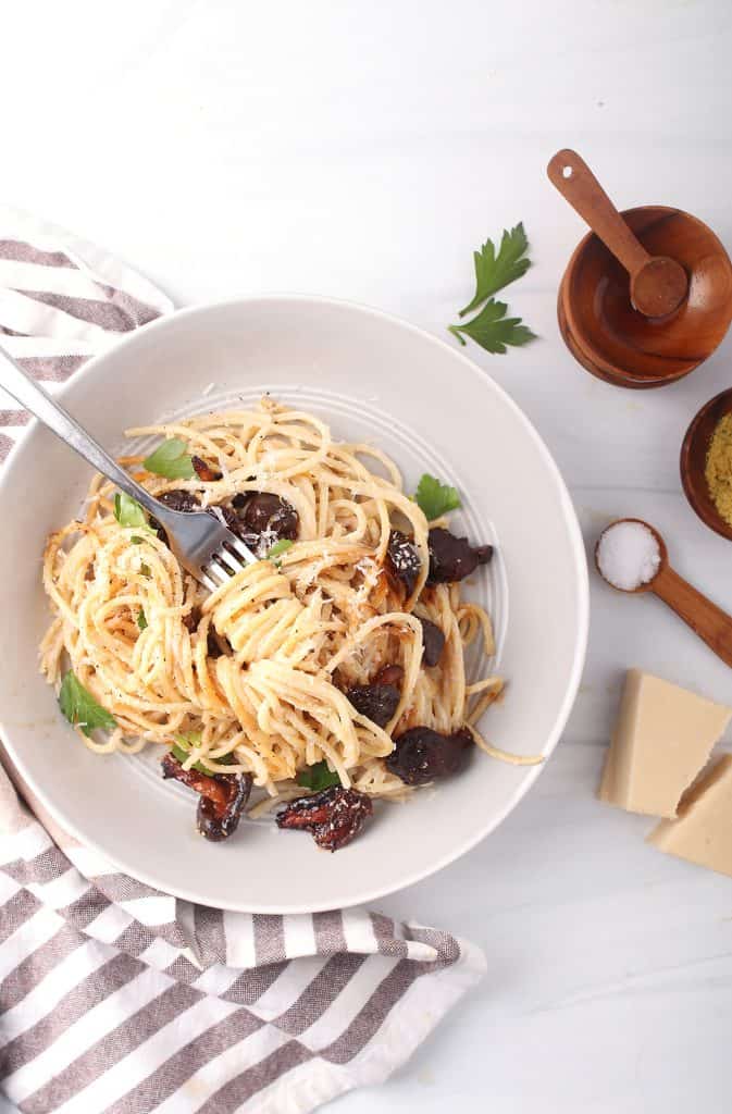 overhead shot of silver fork with a bite of vegan carbonara twirled around it in a white bowl on a white marble table