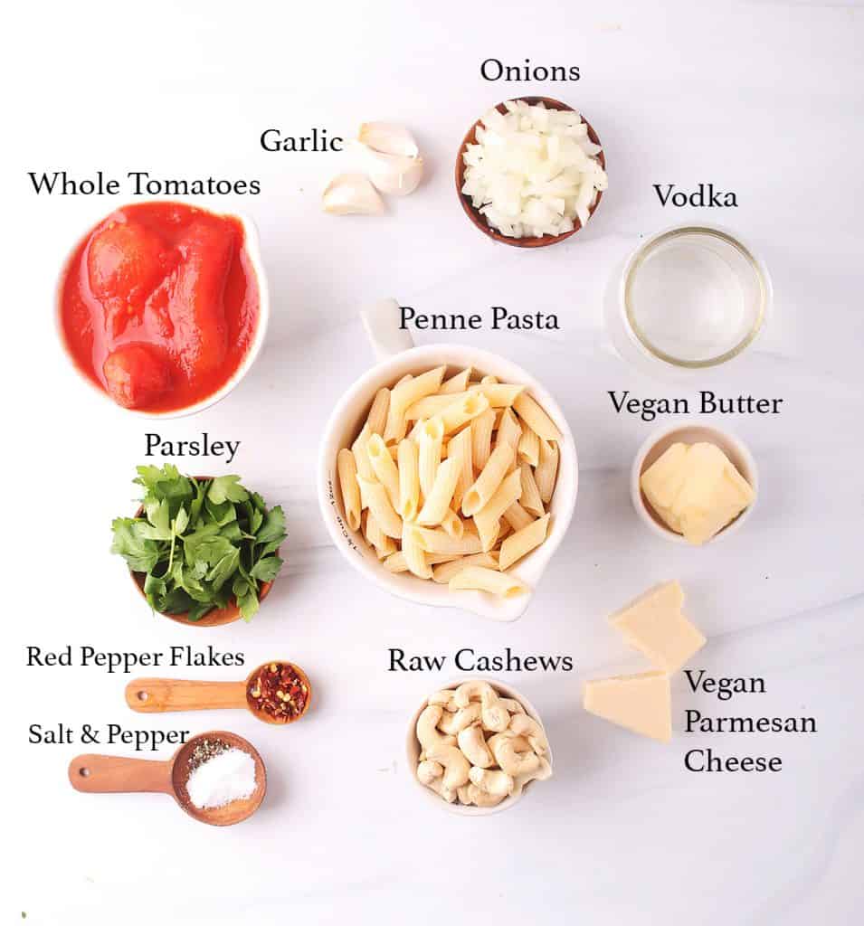 mise en place for penne pasta with vegan vodka sauce - tomatoes, garlic, onions, vodka, penne, parsley, vegan butter, vegan parmesan, red pepper flakes, salt, pepper and raw cashews