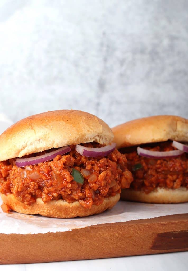 sideways shot of two vegan sloppy joes with meatless crumbles on hamburger buns with red onion
