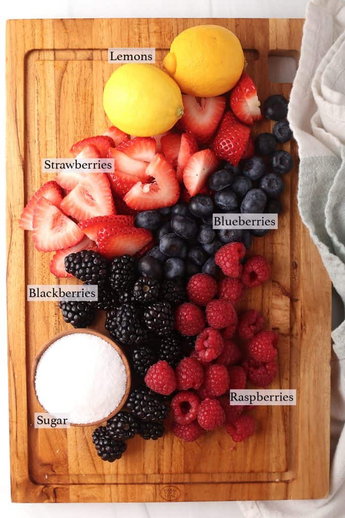 ingredients for vegan mixed berry compote on a wooden cutting board - lemon, mixed berries and sugar