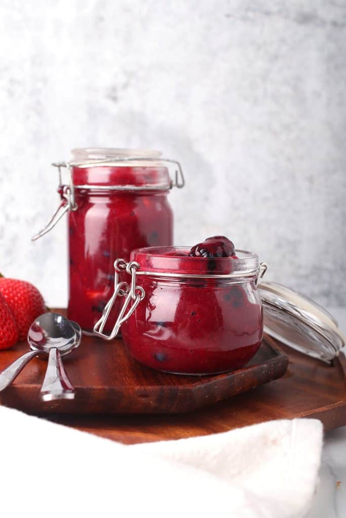 mixed berry compote in a weck style glass preserving can on a wooden cutting board with silver spoons