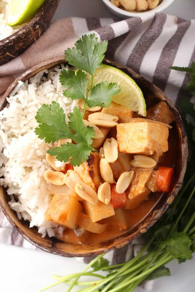 overhead shot of vegan massaman curry with tofu over a bed of rice and garnished with peanuts, cilantro and a wedge of lime