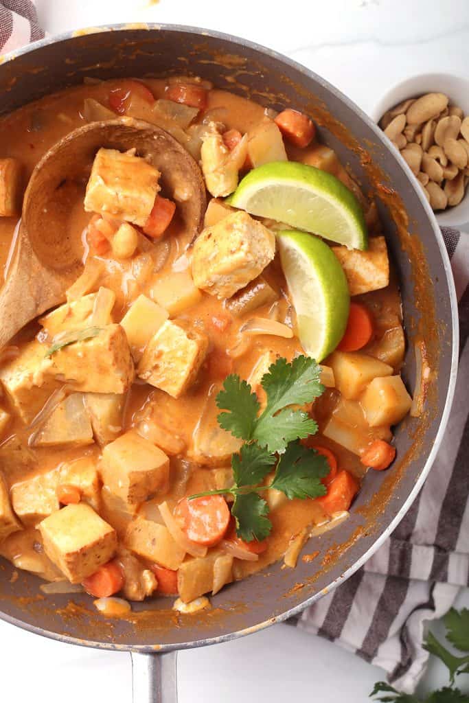 overhead shot of completed vegan massaman curry with tofu in the skillet garnished with fresh cilantro and lime wedges