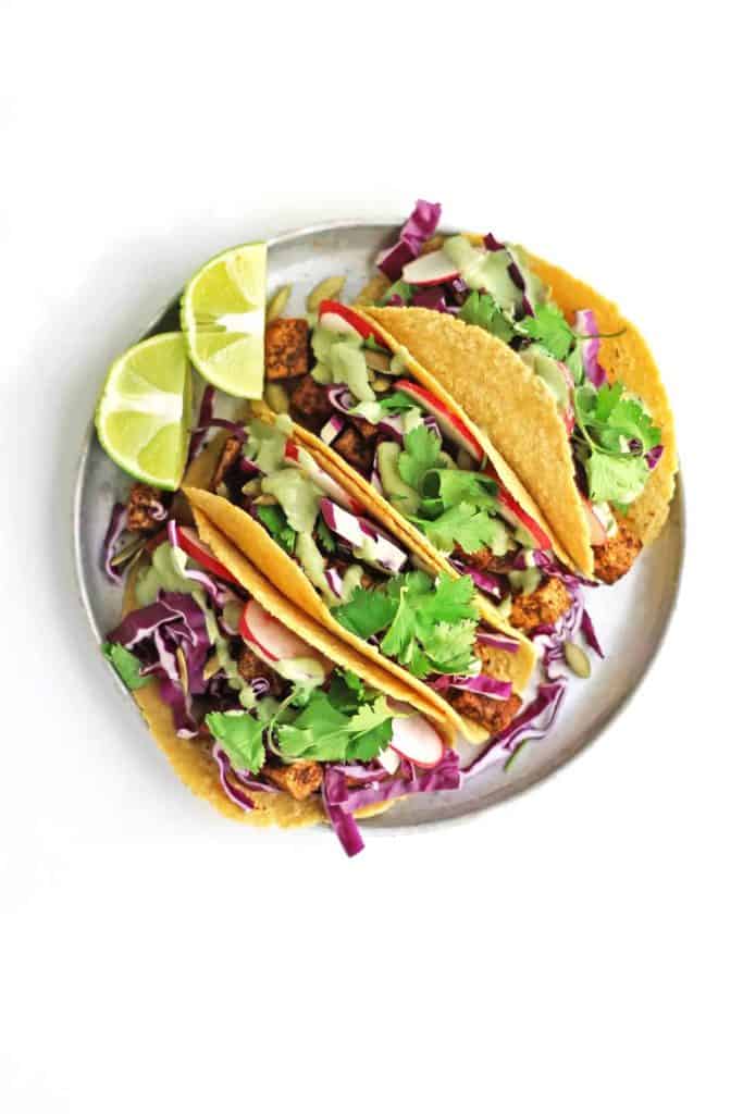 Four Crispy tofu tacos with spicy cilantro crema on a round white plate