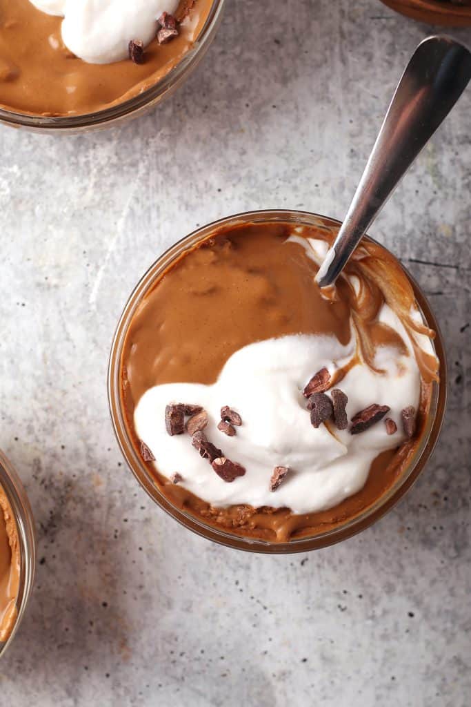 overhead shot of a serving of healthy chocolate pudding with coconut whipped cream and cacao nibs as garnish