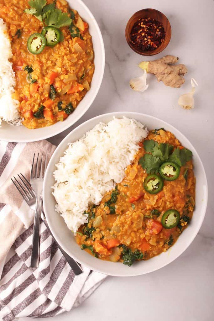 overhead shot of two white bowls filled with long grain white rice and red lentil dahl