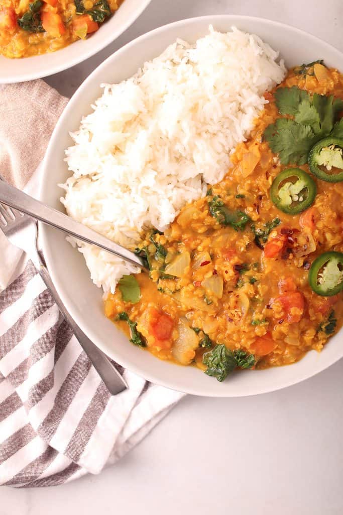 closeup overhead shot of plated red lentil dahl in a white bowl with white rice and a silver spoon