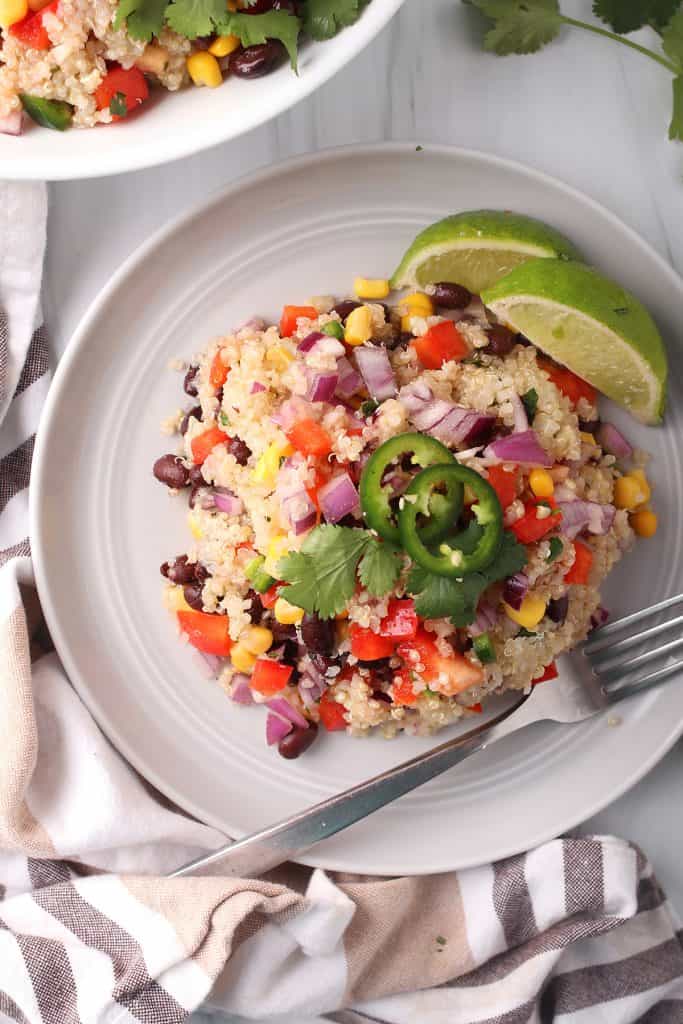 Overhead shot of white plate with a helping of southwest quinoa salad, two slices of lime and garnished with fresh jalapeño and cilantro