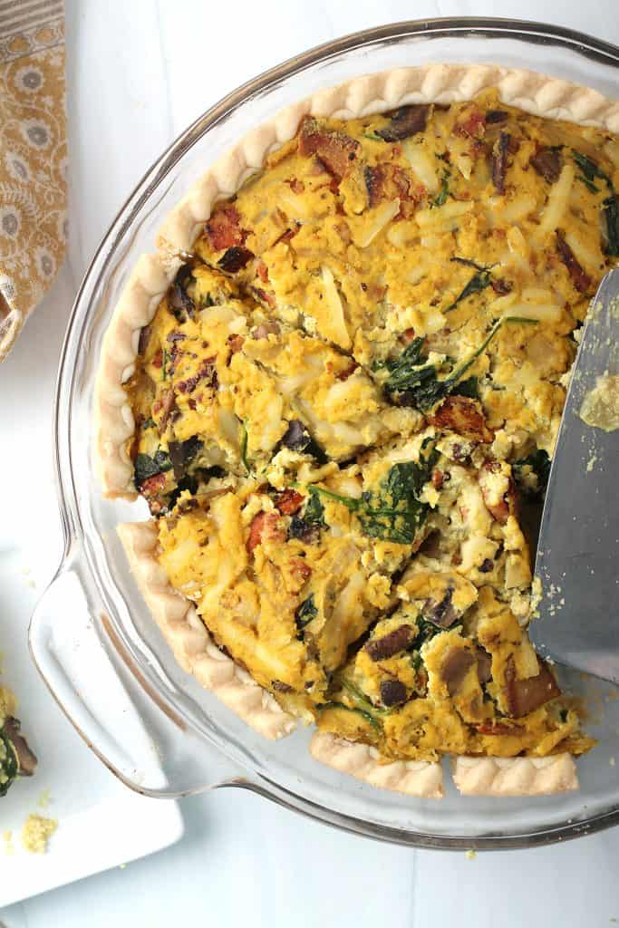 overhead shot of completed vegan quiche lorraine in a clear pie plate with a silver pie server